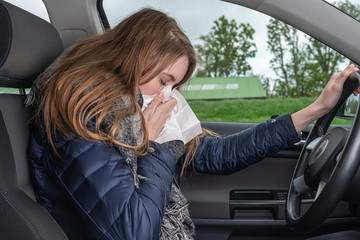A young woman with an allergy sneezes while driving car in a handkerchief