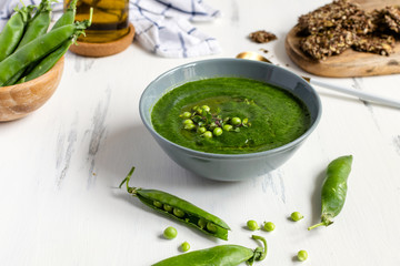 Green peas vegetarian soup in gray bow on white wooden table, seeds crackers - diet food, weight loss