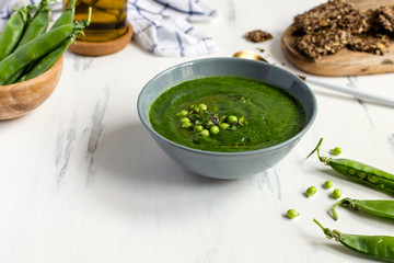 Green peas vegetarian soup in gray bow on white wooden table, seeds crackers - diet food, weight loss
