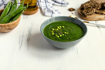 Green peas vegetarian soup in gray bow on white wooden table, seeds crackers - diet food, weight loss