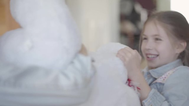 Cute beautiful girl sit in living room on the floor and pulling big white taddy bear