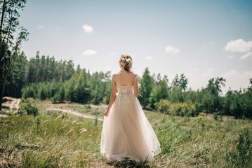 Fototapeta na wymiar a bride in a white dress walks in a green field with a bouquet of flowers in her hands