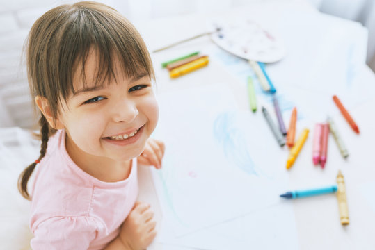 Portrait of happy little girl smiling and drawing with colorful pencils, dressed in pink t-shirt. Pretty preschooler child painting and learning at kindergarten. People, childhood, education
