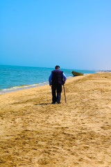 An old man with a cane walks along the beach. Man with a walking stick