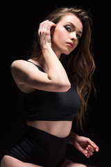Naklejka premium attractive young woman in underwear touching hair and looking at camera isolated on black