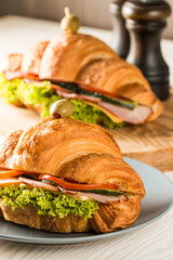 Photo of tasty and fresh croissant sandwich with salad, ham, cheese, tomatoes on wooden background. Morning breakfast concept. Healthy and fast food.