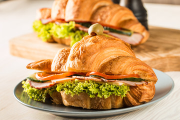 Photo of tasty and fresh croissant sandwich with salad, ham, cheese, tomatoes on wooden background....
