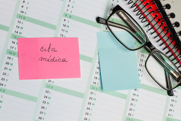 Post it cita médica sobre un calendario junto a una agenda y gafas. Vista superior y de cerca. Copy space