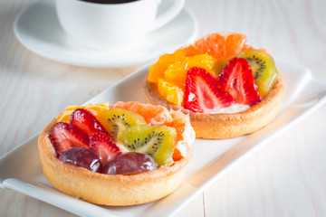 Photo of a fruit and berry tart dessert with toss sugar on wooden background. Fresh delicious sweet cake with raspberries, grapes, strawberries, cherry, kiwi, grapefruit and cream.