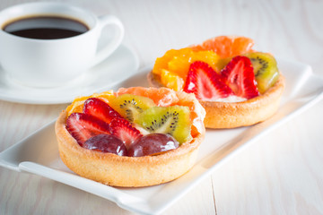 Photo of a fruit and berry tart dessert with toss sugar on wooden background. Fresh delicious sweet cake with raspberries, grapes, strawberries, cherry, kiwi, grapefruit and cream.