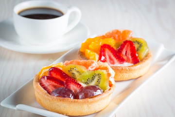 Photo of a fruit and berry tart dessert with toss sugar on wooden background. Fresh delicious sweet cake with raspberries, grapes, strawberries, cherry, kiwi, grapefruit and cream.