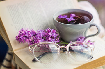 Obraz na płótnie Canvas Book, glasses, cup of tea and lilac on a wooden window. Fragrant tea in the garden. Romantic concept. Vintage style
