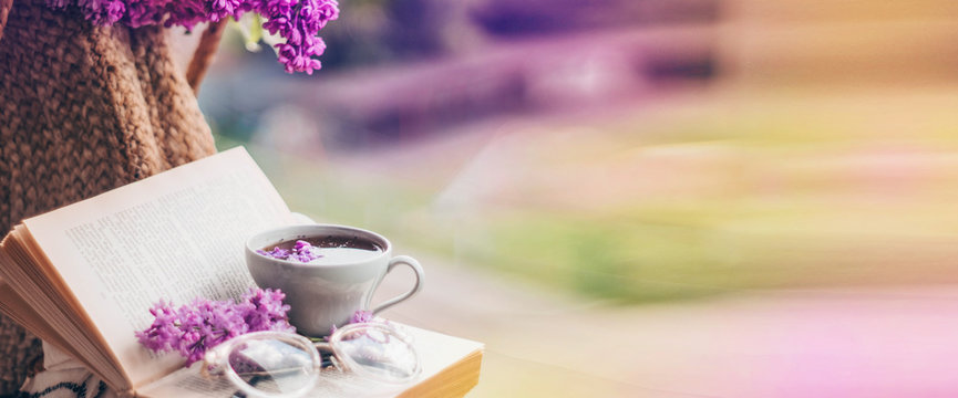 Book, glasses, cup of tea and lilac on a wooden window. Fragrant tea in the garden. Romantic concept. Place for text