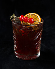 red cocktail with cherry and a slice of dried orange on a black background