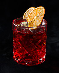 red cocktail with slice of dried orange on a black background
