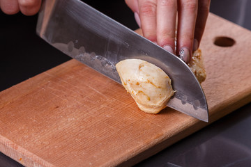 young woman in a gray apron cuts chicken breast