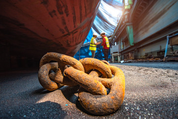 anchor chains bundle laying at bottom layer of the ship in floating dry dock, for recondition maintenance with sand blasting perform, port control and inspector surveying condition in background © ID_Anuphon
