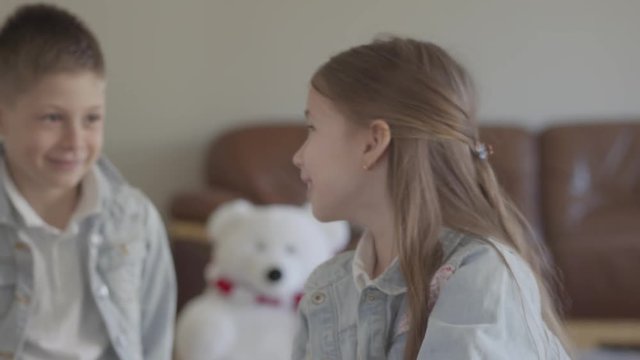 Twin brother naughty boy playing pulling the hair of his cute sister and smiling in cozy living room