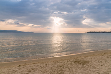 Fototapeta na wymiar Sunbeams or sun rays peeking through the clouds at a sunrise on beautiful beach