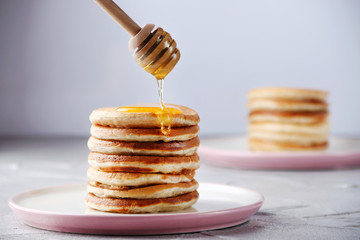 Stack of Pancakes with honey spoon and pouring honey on light background