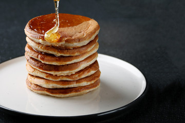 Stack of Pancakes with pouring honey on dark background. honey spoon