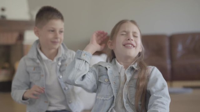 Portrait adorable twin brother naughty boy playing pulling the hair of his cute sister and smiling in cozy living room