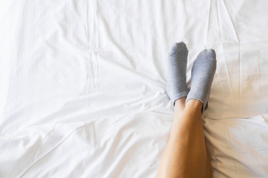 Woman legs on the bed in white bedclothes. Close up of young woman lying in bed at home. Fest, sleeping, comfort concept with copy space.