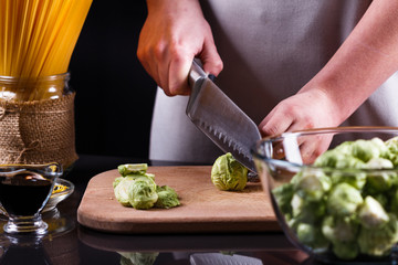young woman cuts Brussels sprouts on a wooden cutting board