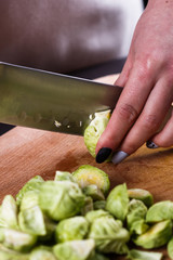 young woman cuts Brussels sprouts on a wooden cutting board