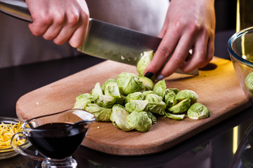 young woman cuts Brussels sprouts on a wooden cutting board