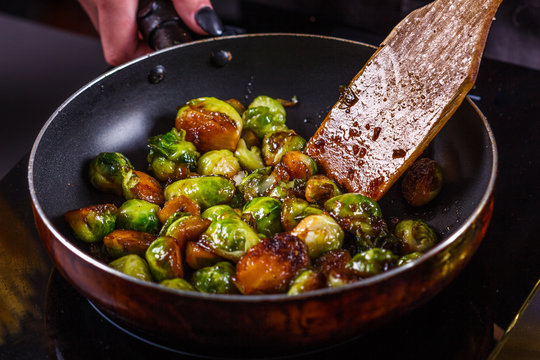 young woman fries Brussels sprouts on a frying pan