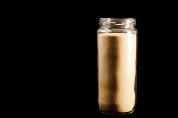 Couscous groats in a round glass jar on a black background, isolate.