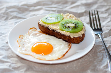 Delicious and healthy breakfast. Fried eggs and kiwi sandwich on white plate