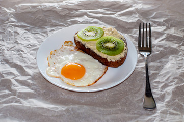 Delicious and healthy breakfast. Fried eggs and kiwi sandwich on a white plate, close-up, space for text