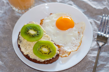 Healthy and tasty breakfast, juice, wholegrain sandwich with kiwi and fried egg on white plate
