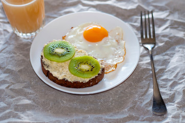 Healthy and tasty breakfast, juice, wholegrain sandwich with kiwi and fried egg on white plate