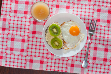 Healthy, tasty breakfast, quince juice, whole-grain bread sandwich with kiwi and fried egg on white plate, view from top