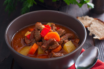 Pot of hungarian goulash on rustic wood background with chili peppers and laurel and copy space