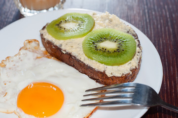Healthy, tasty breakfast, juice, whole-grain bread sandwich, kiwi and fried egg on a white plate, on wooden table