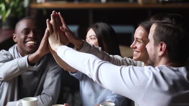 Diverse young happy friends join hands giving high five together