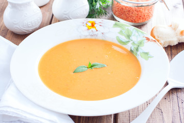 Red lentil cream soup in a white plate on a wooden table, horizontal