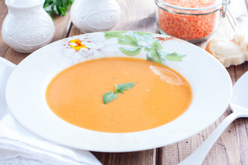 Red lentil cream soup in a white plate on a wooden table, horizontal