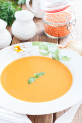 Red lentil cream soup in a white plate on a wooden table, selective focus
