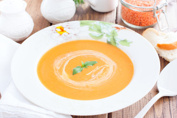 Red lentil cream soup in a white plate on a wooden table, horizontal