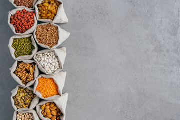 Small burlap sacks with almond, chickpeas, walnuts, buckwheat, raisins, goji against grey background with copy space for your advert