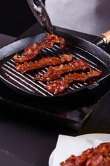 young woman in a gray apron fries bacon