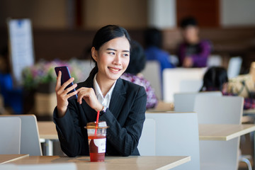 Young beautiful female wears black business suit works, shops online via cell phone and laptop with happy and smile face in department store. Business person, modern lifestyle, and shopping concept.