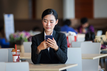 Young beautiful female wears black business suit works, shops online via cell phone and laptop with happy and smile face in department store. Business person, modern lifestyle, and shopping concept.