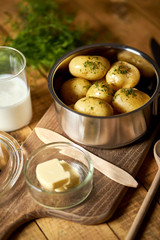 Young potatoes boiled in  pot with dill and butter on wooden board