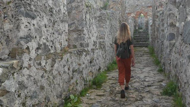 Woman tourist walking on ancient castle wall to shoot a picture with calm Mediterranean sea on background.